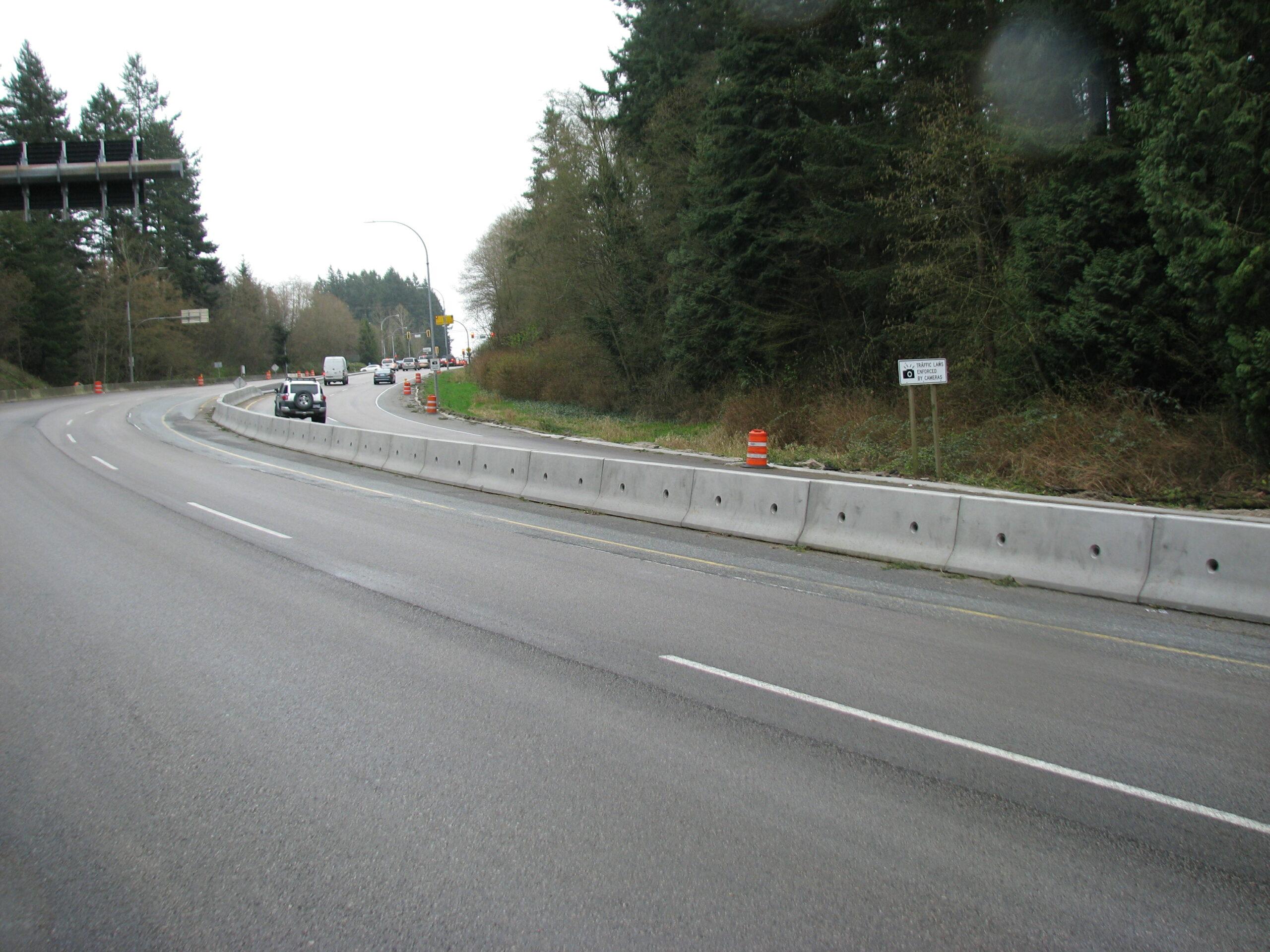 A line of Jersey barriers hugs a curve in a roadway as motorists drive past.