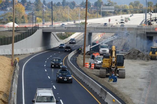 Concrete barriers cordon off an active construction zone as cars drive on a roadway underneath an overpass.